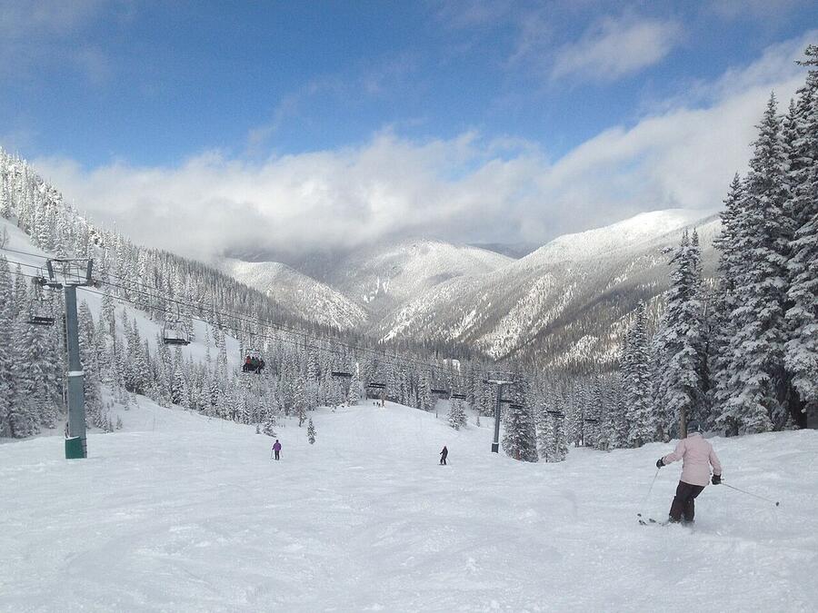 Skiers on a snowy run at Taos Ski Valley, surrounded by forested peaks